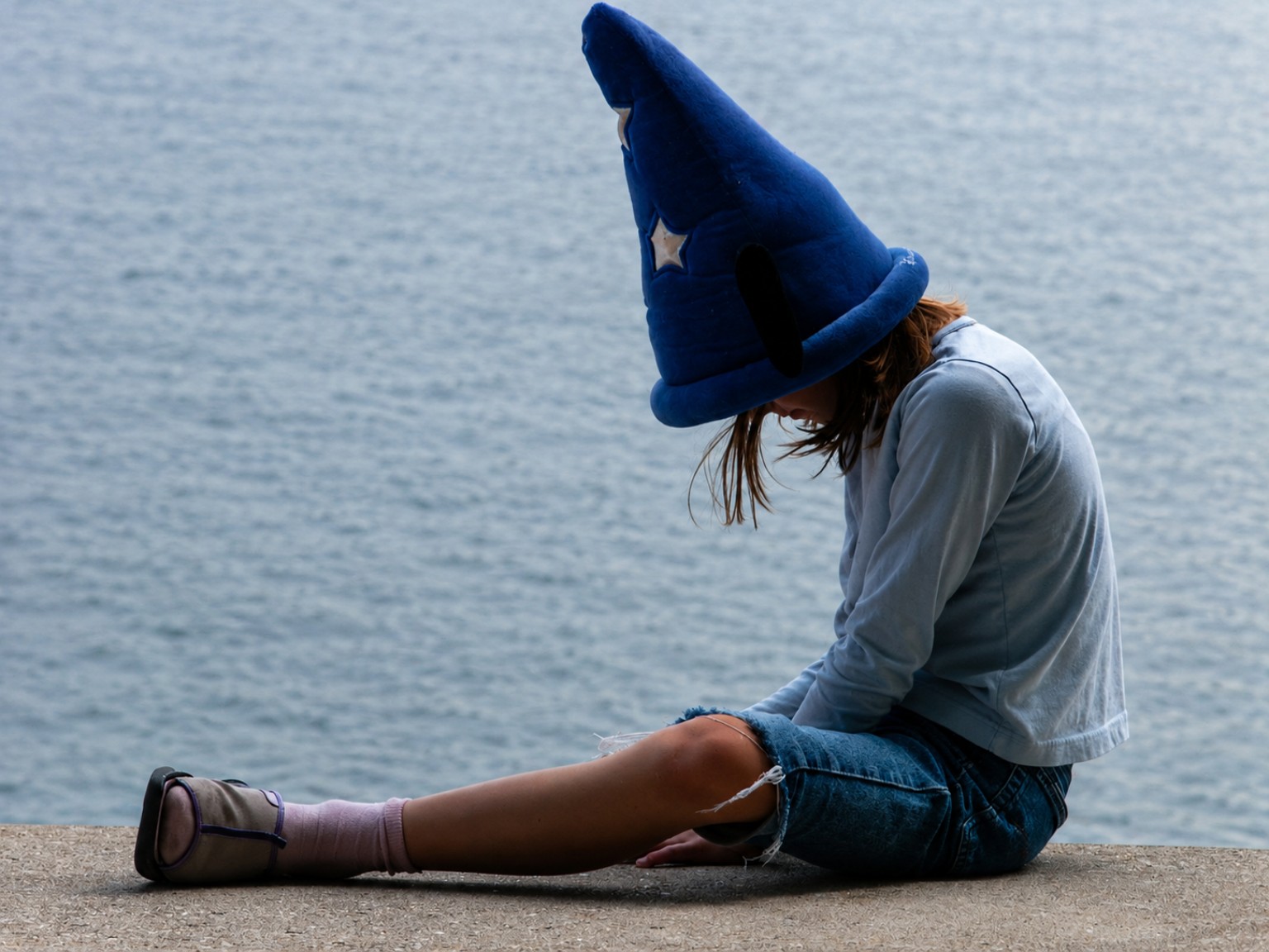 A person wearing an oversized blue wizard hat beside the water